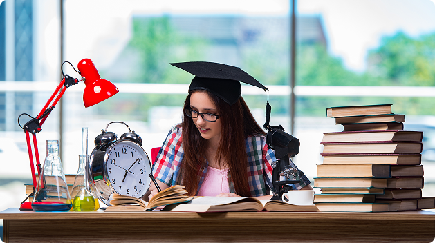A nursing student in a graduation cap studying TEAS science section with books, lab equipment, and a clock on her desk